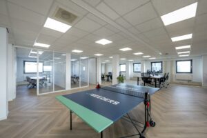 Modern kantoorpand aan de Joan Muyskenweg met glazen vergaderruimtes, werkplekken en een tafeltennistafel van Seeders op de voorgrond.